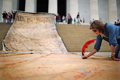 A woman signs a giant banner printed with the Preamble to the United States Constitution during a demonstration against the Supreme Court's Citizens United ruling at the Lincoln Memorial on the National Mall October 20, 2010, in Washington, D.C. The rally at the memorial was organized by brothers Laird and Robin Monahan who spent the last five months walking from San Francisco, California, to Washington to protest the court decision, which overturned the provision of the McCain-Feingold law barring corporations and unions from paying for political ads made independently of candidate campaigns.